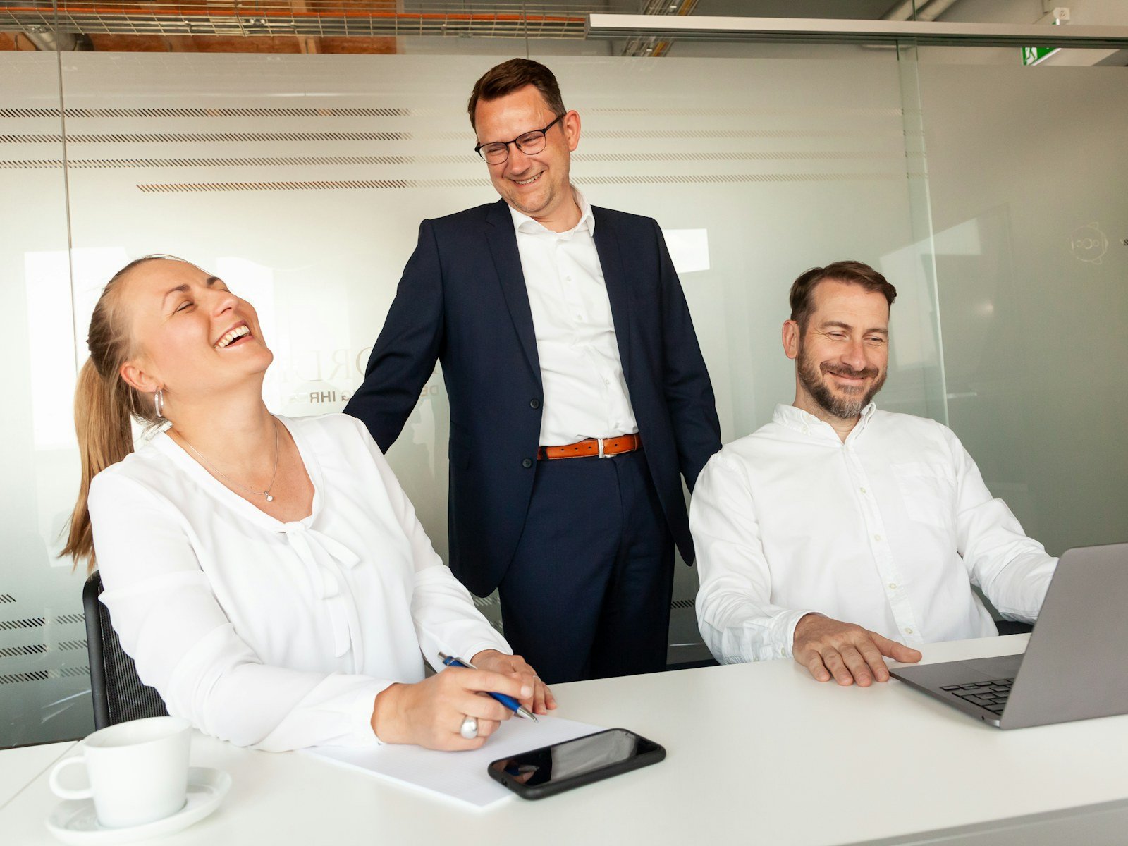 Three colleagues laughing together at a table in a bright office
